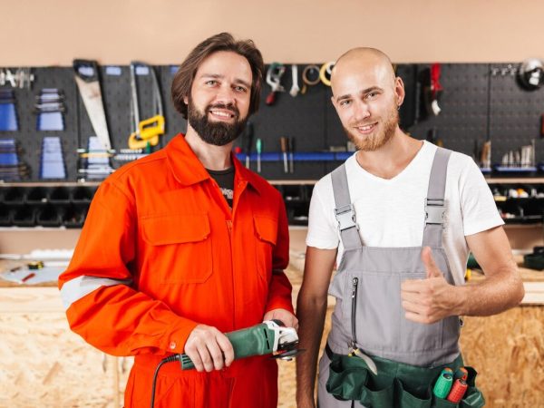 two-smiling-builders-work-clothes-happily-looking-camera-spending-time-workshop-with-variety-tools-background_574295-1638